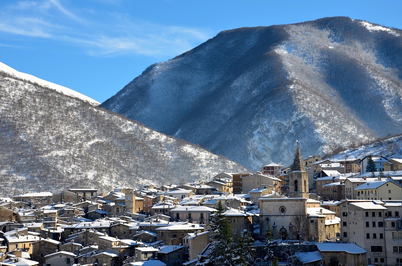 Panorama di un borgo montano italiano coperto di neve, con case in pietra e paesaggio innevato.