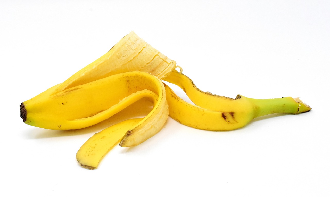 Bucce di banana a terra vicino a rose fiorite, metodo naturale per potenziare la fioritura.